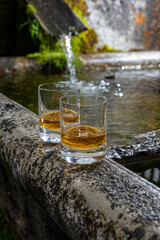 Glasses of strong scotch single malt whisky served on old stone reservoir for water from mountain spring