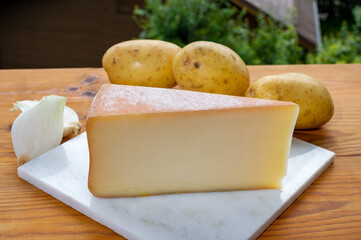 Tastes of Savoia, French cow cheese for gratin abondance, potatoes and french mountains village in Haute-Savoie on background
