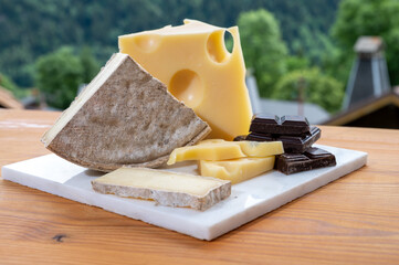 Cheese collection, Swiss cow cheese emmental, tomme and dark chocolate and mountains village in...