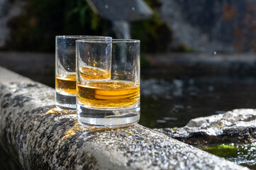 Glasses of strong scotch single malt whisky served on old stone reservoir for water from mountain spring
