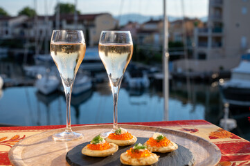 Russian style party with two glasses of white cold champagne, bliny with red caviar and view on Port Grimaud near Saint-Tropez in summer
