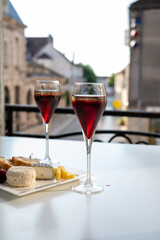 Drinking of Kir Royal,  French aperitif cocktail made  from creme de cassis topped with champagne, typically served in flute glass, with view on old French village
