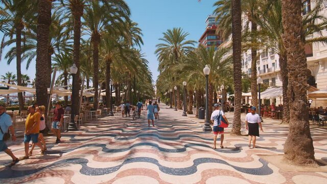 Benidorm, Spain 18.08.2021 Alley Of Palm Trees in Spain along the Mediterranean Sea. Small Market. Tourists walking on the street with palm trees on the sides of the road. SlowMotion footage on a