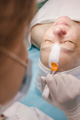 A woman aged at the reception of a beautician. Facial care, skin cleansing and wrinkle elimination. Facial treatment, application of the mask with a brush
