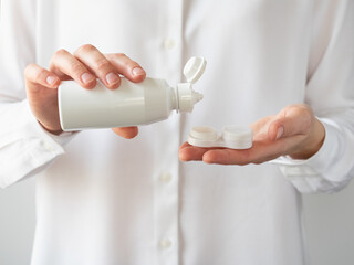 A woman pours a contact lens solution into a contact lens container.