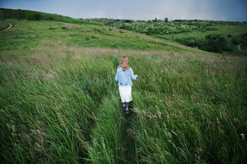 Kid stands along in grass on hilltop, looks into distance. Girl walks in open air. Childhood, freedom, enjoy life, dream, future vision concepts. Copy space.