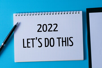 2022 let's do this written in a notebook on blue background with pen and paper on clipboard.