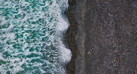Dramatic stormy waves with white sea foam over black sand beach, aerial sea texture