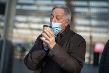 Covid coronavirus concept, masked elder man drinking coffee outdoor