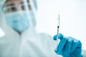 Unrecognizable specialist doctor in a medical PPE suit showing and looking at an injection needle.
