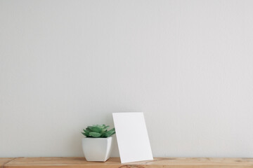 Empty postcard paper mockup with cactus pot on white wall.