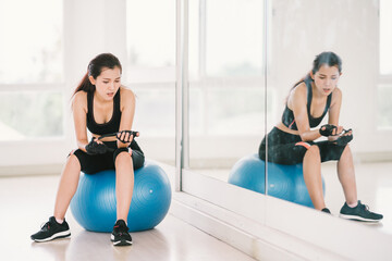 Young, determined Asian woman exercise alone at home gym or sports club, sit on fitness ball with...