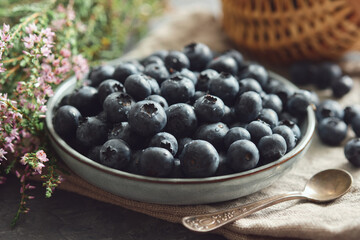 Blue plate of fresh blueberries and heather flowers on kitchen table.