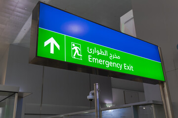 Emergency exit sign in English and Arabic glowing green at airport	