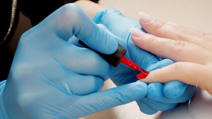 Manicurist paints nails with red gel polish. Nail polish application. Manicured red nails.