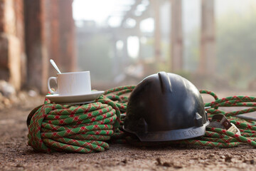 A white cup of coffee stands on a rope against the blurry background of an industrial zone. On the...