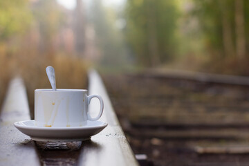 A white cup with a spoon is standing on a railway car. Coffee on the railway. A cup of tea on the...