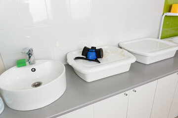 Obraz na płótnie Canvas Sink and enameled containers for washing disinfection in the clinic room for processing reusable medical equipment and instruments. A respirator and goggles to protect against chemical fumes