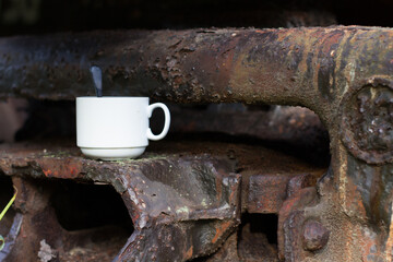 A white cup with a spoon is standing on a railway car. Coffee on the railway. A cup of tea on the railway.