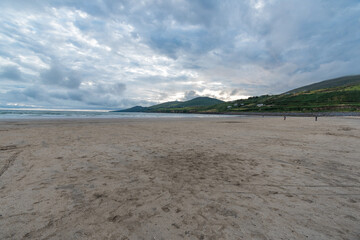 Overcast sky over sands of a beach with tide out. Mauntains in the distance.