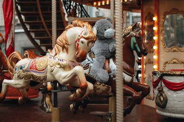 Children ride horses and teddy bear in protective mask on children's carousels in an amusement park.
