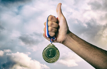 Medal gold in winner hand. First place award, sky background. Sport champion athlete victory concept