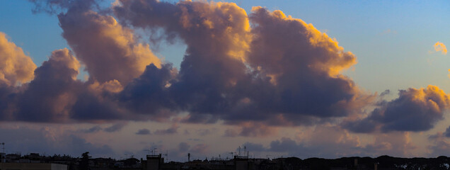 Backlit profile of the city and vast sky filled with dark clouds reddened by the sunset light.