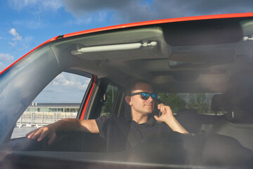 A middle-aged man with glasses speaks on the phone in the car