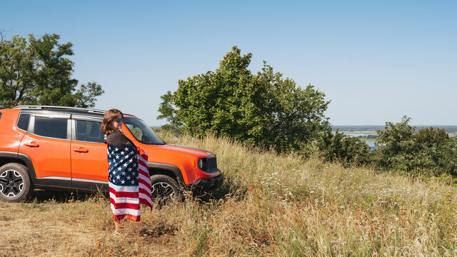 Happy woman with the flag of America near the car enjoying the sunset in nature - Powered by Adobe
