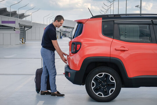 A Man With Luggage Opens The Trunk Of A Car In An Open Parking Lot