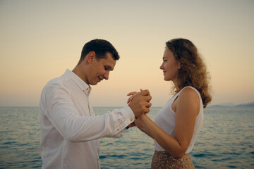 Young adult heterosexual couple at romantic date. Young adult man and woman holding hands looking to each other. Seaside romantic walk