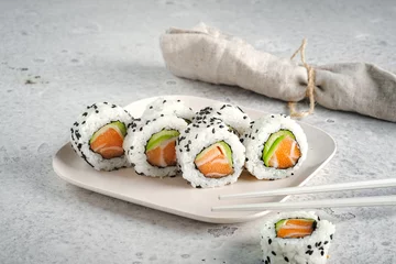 Foto op Plexiglas A set of fresh sushi rolls with salmon, avocado and black sesame seeds served on a plate with chopsticks. Japanese sushi uramaki or California roll © Andrey