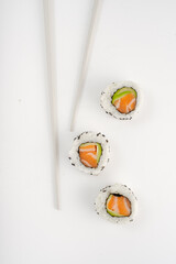 California sushi roll with salmon and avocado on isolated on white background with chopsticks