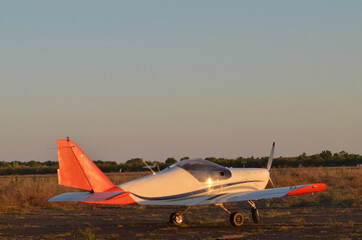 A small plane standing on the ground, illuminated by the autumn sun.

