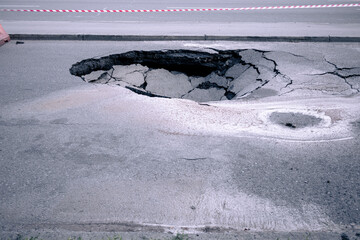 A large pit in the asphalt due to a pipeline accident. A hole in the ground in the middle of the road © Klochkov