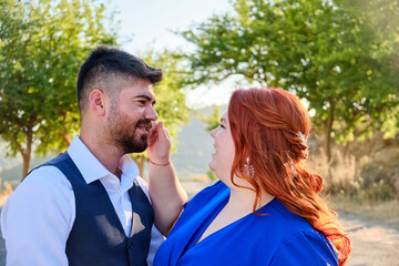 Gorgeous happy caucasian plus size red headed woman touches her husband smiling. Mixed race couple engagement. Middle eastern man and caucasian woman hugging.