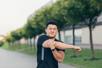 Male asian athlete, kneading shoulder pain, sore arm muscles in the park