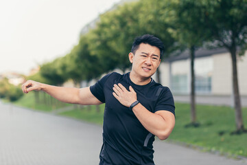 Fototapeta na wymiar Male asian athlete, kneading shoulder pain, sore arm muscles in the park