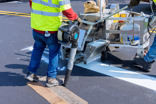 Road worker painting white line on the street surface tor thermoplastic spray marking machine during road construction