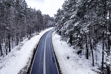 Asphalt road leading through the snowy forest. Transportation in winter.