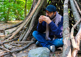 Young man in the forest drinking coffee under a shelter