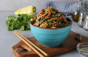 Korean style eggplant salad with sesame seeds, onions and carrots in a blue bowl on a gray...