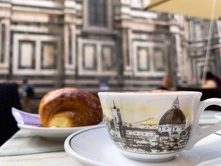 Latte art coffee cup with croissant and historical building in the background.