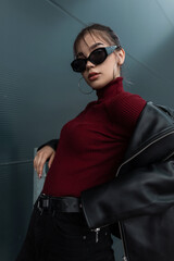 Cool young stylish woman in fashion sunglasses with a stylish black leather jacket and a burgundy...