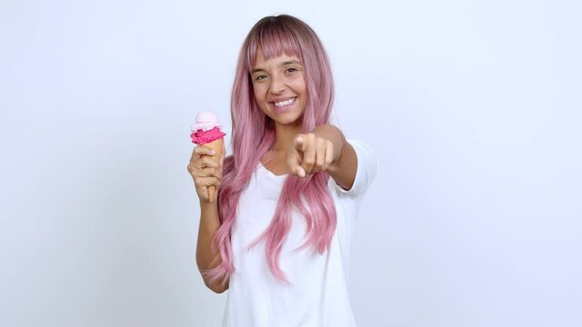 Young woman with pink hair holding a cornet ice cream points finger at you with a confident expression over isolated background