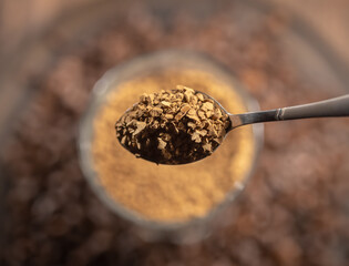 Metal spoon of instant coffee on a dark coffee background
