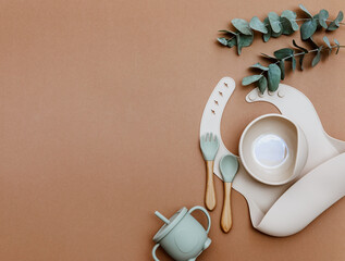 Baby food accessory on brown background. Neutral silicone bib and bowl. Kids dishware kit, serving...