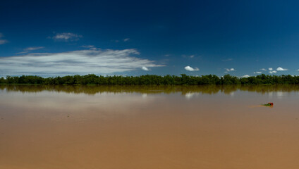 Symmetry in nature. Panorama view of the brown water Parana river under a clear blue sky. View of the wide river and jungle reflection in the water.