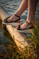 Young lady legs while she is sitting on pier lit by setting sun