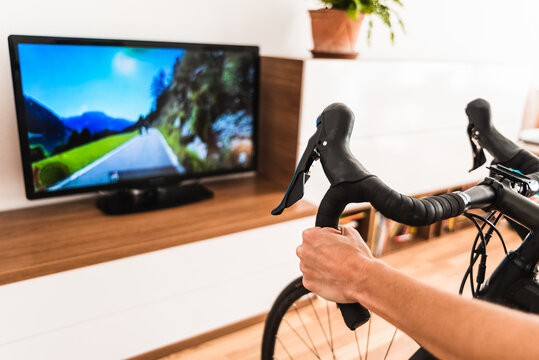 Woman play online bike game in the living room of her home, sweating while doing pedaling exercise connected to the internet on her smart tv.